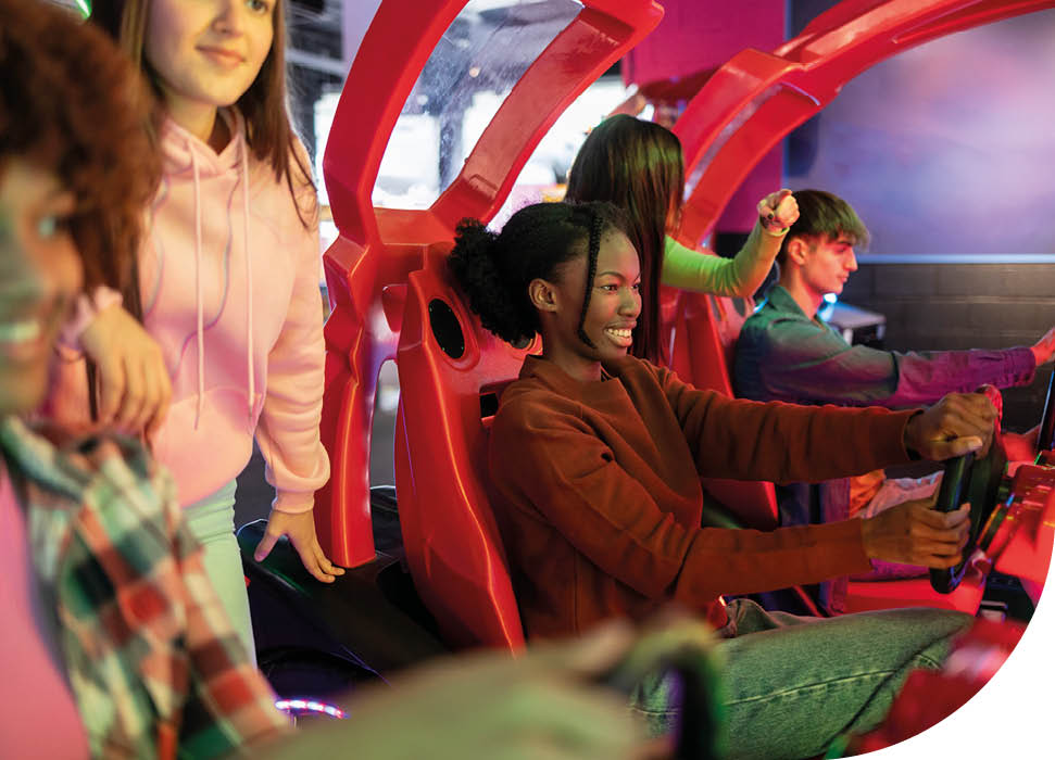 Group of young friends playing an exciting racing game at an arcade, enjoying the thrill and friendly competition.